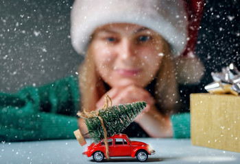 a Christmas tree tied to a toy car on a table, a girl dressed in a Santa hat is dreamily looking at a typewriter.