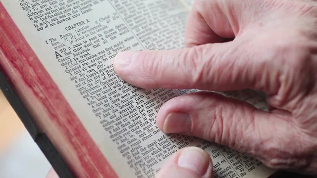 Older man holds a vintage Bible, and uses his index finger to track the words of the Christmas story