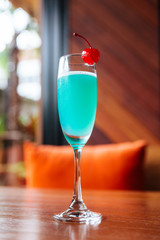 Turquoise color cocktail served with fresh cherry.