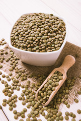 Green lentils in a bowl on a wooden background.