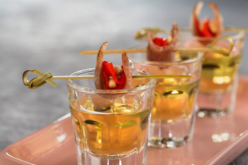 Close-up shot of three glasses of Golden tequila with tapas on skewers with dried meat, baked bell pepper and pine nuts.