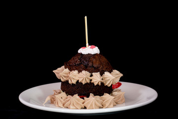 Fresh baked chocolate cake with whipped cream around on white plate with isolated black background