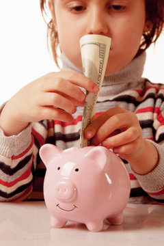 Keep money at the bank concept. Portrait of cute little business child girl with piggy coin bank and US Dollar bills.