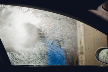 man washing automobile manual car washing self service,cleaning with foam,pressured water. Washing car in self service station with high pressure blaster window viewed from inside car