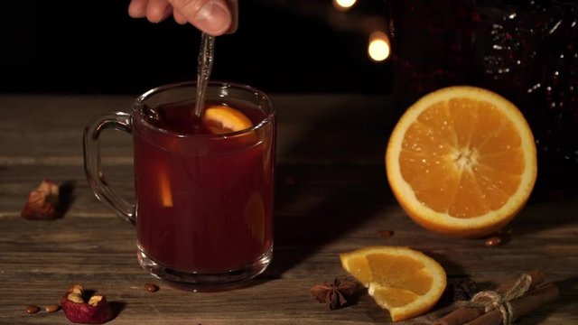 Close-up of a mug with mulled wine. Male hand stir drink with oranges