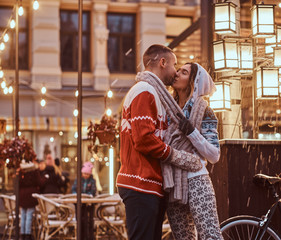 A young romantic couple wearing warm clothes holding hands and kissing standing outdoors at night, enjoying spending time together.