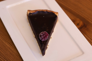 Fresh baked chocolate tart with raspberry on top served on white plate with isolated black background