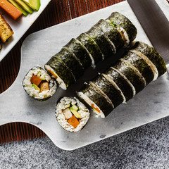 vegan ready-made sushi on the table in fish plates. rolls with fried tofu, cucumber, boiled carrots and fresh avocado. healthy vegan food