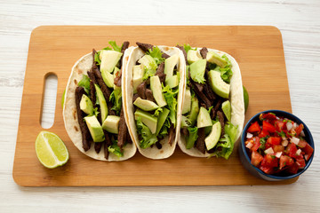 Corn tortillas with grilled beef, avocado, lime and salsa on bamboo board, side view.