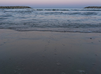Fototapeta premium a nice sunset scene of a the sea beach and Groynes with a sea water splashing against them as they down the pebble beach and disappear into the blue sea water of the Herzliya beach