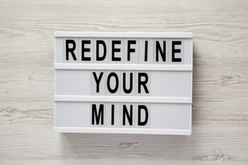 'Redefine your mind' words on lightbox over white wooden surface, top view. Overhead, flat lay, from above.