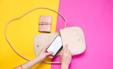 Women's hand takes smartphone from leather bag on colored paper background. Top view, flat lay,...