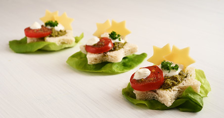 creative party canapes on lettuce with tomato, pesto and cheese in star shape for christmas or new year, light background with copy space