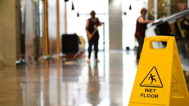 Yellow warning sign wet floor. Sign showing warning of caution wet floor and workerw cleaning hall floor of  business building.