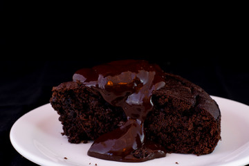 Fresh baked chocolate fudge cake with chocolate dressing on white plate with isolated black background