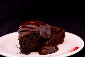 Fresh baked chocolate fudge cake with chocolate dressing on white plate with isolated black background