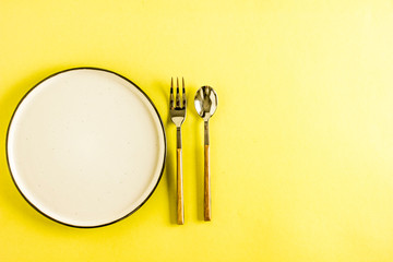 Empty plate with cutlery spoon and fork on yellow background close-up. 