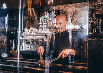 Chef cooking delicious beef steak on a kitchen, standing behind protective glass in a restaurant.