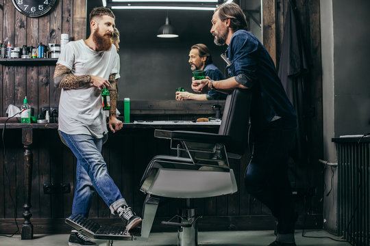 Two bearded men drinking beer while talking in barbershop
