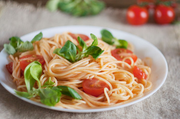 pasta in a plate on a wooden table .. under a plate napkin of flax. near cherry tomatoe