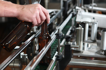 Hand worker puts an empty beer bottle on the conveyor of the plant for the production of beer. Only the bottle is in focus. Man's hand close-up.The concept of production.