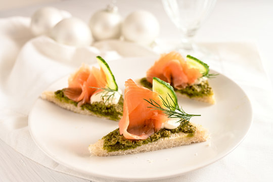 festive canapes with smoked salmon, pesto, cucumber and dill garnish, white table cloth and christmas decoration, copy space