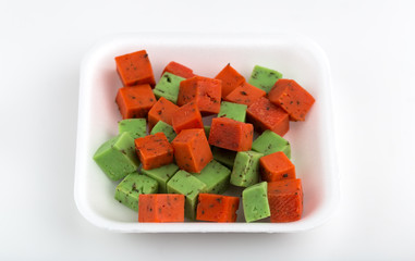 Cheese pesto in a plastic container. Cheese cubes of red and green color in the container from the store on a white background.