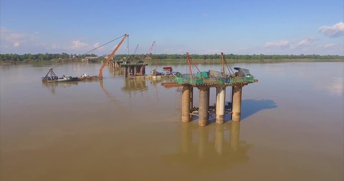 aerial slider shot of bridges foundations and  barges mounted cranes in river 