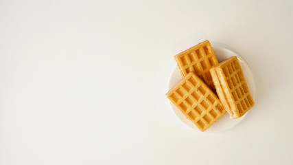 Light waffles on a white saucer.  Light background. The view from the top. Tasty and appetizing. Minimalism. Place for text.