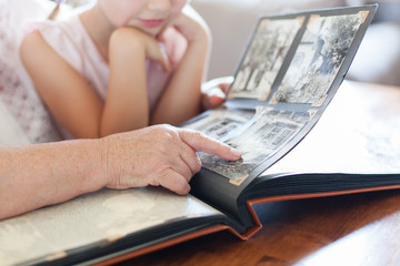 Grandmother and granddaughter watching old photo album at home. Senior woman shows child black and white photos. Hands of retired person and kid. Family leisure. - obrazy, fototapety, plakaty