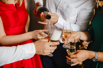 Hand pouring champagne from bottle into glasses with friends around him. Closeup of hand pouring white wine in flutes during party. Detail shot of new year’s eve celebration.