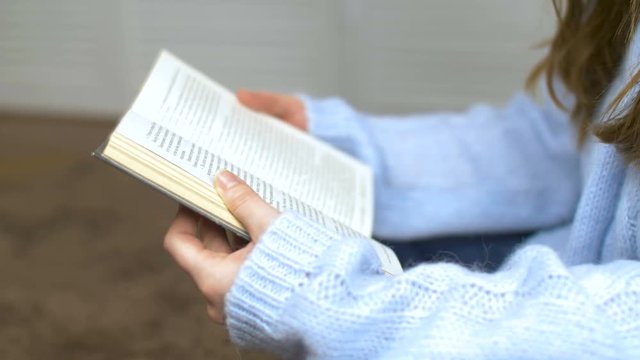 Young girl in a blue sweater read book in slow motion. Close up.