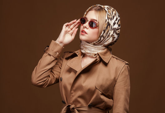 Portrait of young beautiful woman in trendy trench coat over beige background. Elegant fashion look.