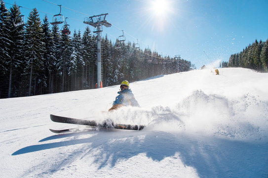 Skier falling on the slope on fresh powder snow at winter resort. Blue sky, sun and winter forest on the background copyspace adventure extreme adrenaline active lifestyle concept