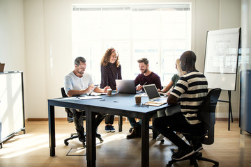 Smiling group of designers talking together around an office tab