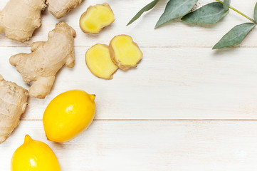 Whole and sliced fresh ginger roots, eucalyptus, lemon on white wooden background top view copy space. Seasoning, spice, ingredient for tea. Concept healthy food, medicine, improving immunity