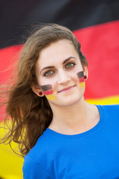 Happy young woman with German flag on cheeks  on the background of the German flag/ Happy young woman with German flag on cheeks. Cheerful multiracial woman in Germany travel concept.