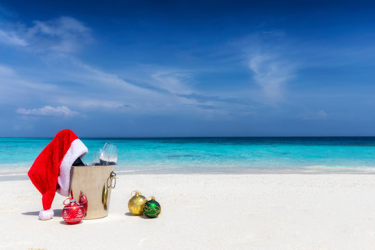Weihnachten in der Karibik: Champagner Kübel mit roter Weihnachtsmütze und Christbaumkugeln im Sand