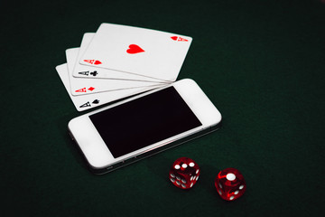 Side view of a green poker table with a smartphone, cards and dices. Gambling app addiction..