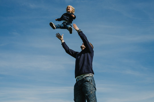 .Funny father playing with his son in the park on a sunny autumn day. Throwing him into the air, making him fly while the kid laughs. Lifestyle