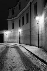 Narrow snow covered street in historic city of Prague. Empty street and car tracks on cobblestoned street. Monochrome night image