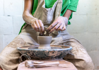 Cropped close up photo of focused lady in her workwear she sit indoor workspace make ceramics small tea cup by hands using special tool