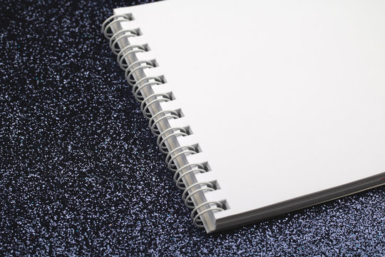 White notebook with blank sheets on black.