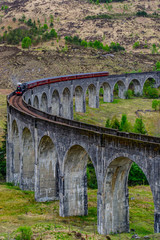 Fototapeta premium Wiadukt Glenfinnan, Szkocja. Podróż / miejsce turystyczne w Europie. Stary historyczny pociąg parowy jazda na scenie filmowej słynny wiadukt most. Highlands, góry, tło na zewnątrz.