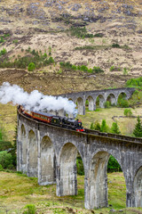 Glenfinnan Viaduct, Scotland. Travel/tourist destination in Europe. Old historical steam train riding on film scene famous viaduct bridge. Highlands, mountains, outdoor background.