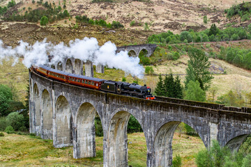 Glenfinnan Viaduct, Scotland. Travel/tourist destination in Europe. Old historical steam train riding on film scene famous viaduct bridge. Highlands, mountains, outdoor background.