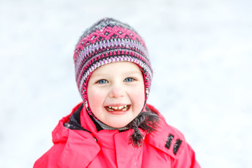 Fototapeta na wymiar A pretty white girl in a knitted winter hat and pink jumpsuit, smiling and laughing in the snow . Portrait close-up.