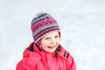 A pretty white girl in a knitted winter hat and pink jumpsuit, smiling and laughing in the snow . Portrait close-up.