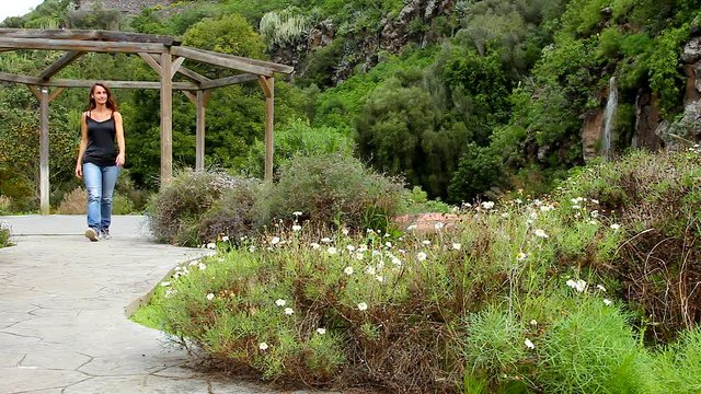 Young woman walking in park in Gran Canaria island, Spain. Beautiful lady in blue jeans and black tank top enjoying nature in Jardin Canario