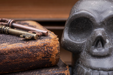 Pile of antique hard cover books, old vintage metallic keys and carved skull on natural stone background